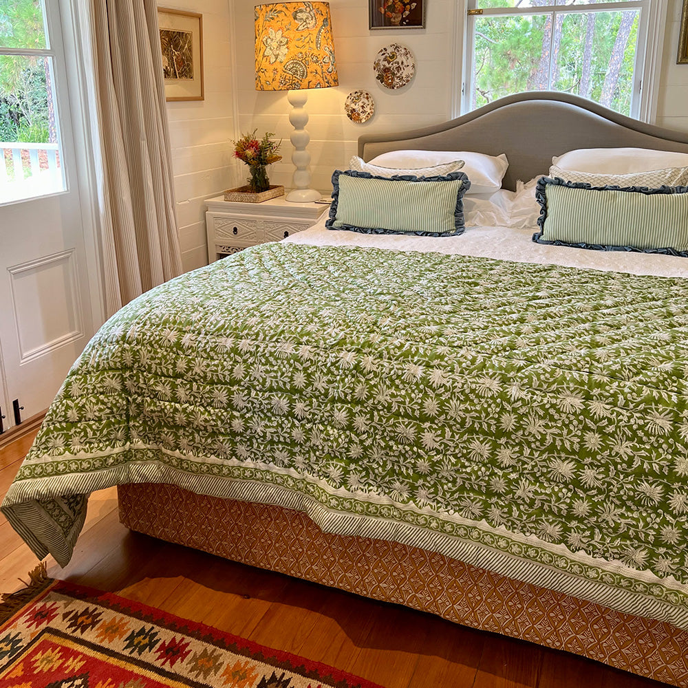 Photo of a forest green and white floral quilted bedspread over the end of a bed.