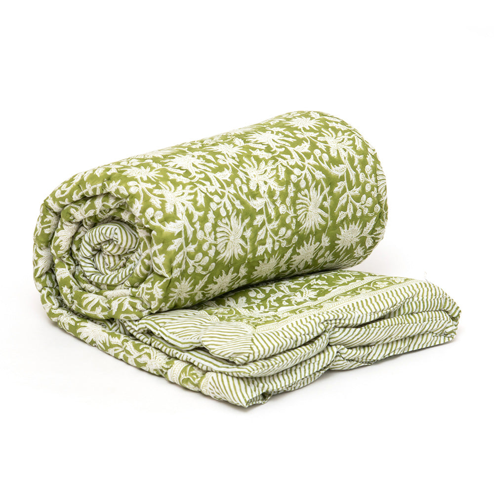 Photo of a forest green and white floral quilted bedspread rolled up with just the end showing which shows the reverse pattern of the quilt being forest green and white stripe.