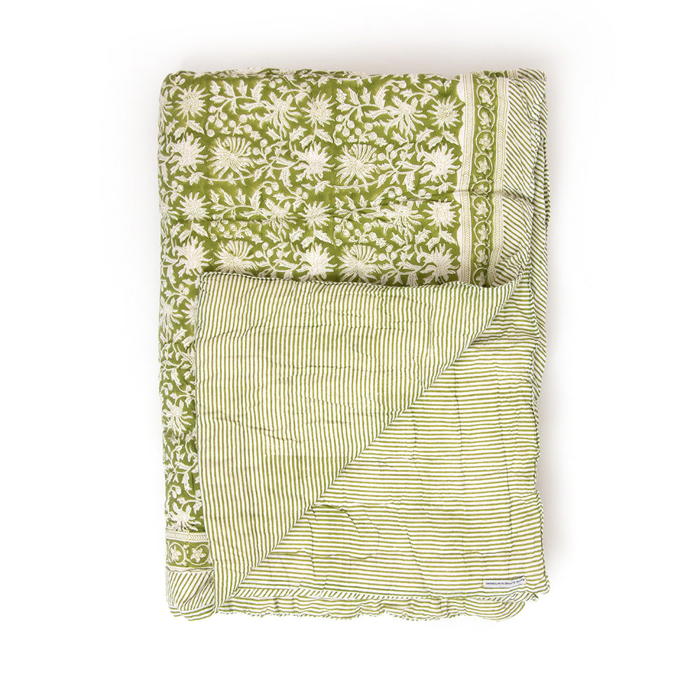 Photo of a forest green and white floral quilted bedspread folded up with one corner turned upwards which shows the reverse pattern of the quilt being forest green and white stripe.