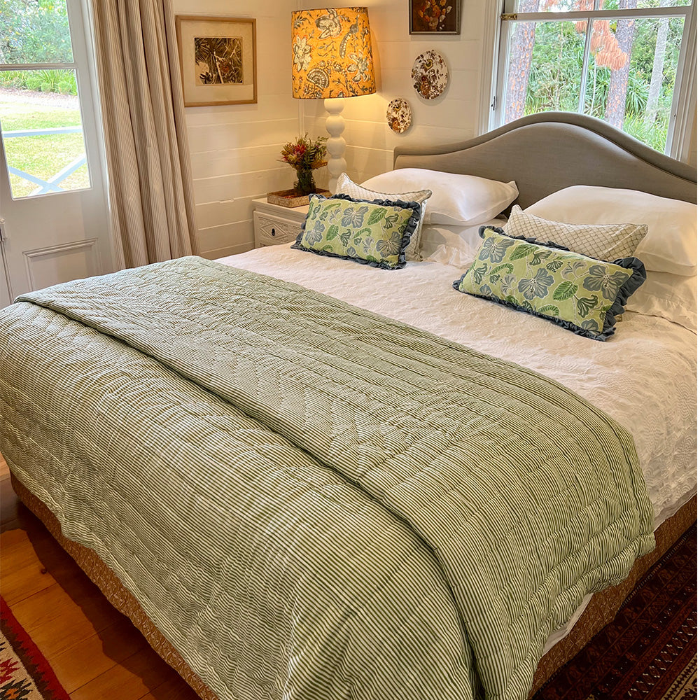 Photo of a forest green and white striped quilted bedspread over the end of a bed.