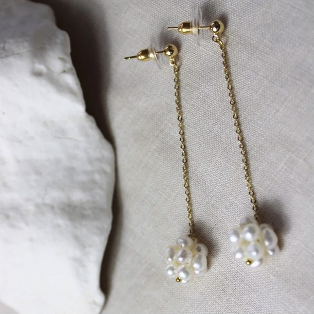 Photo of gold stud earrings with an attached fine gold chain and a cluster of small freshwater pearls at the end of the chain.