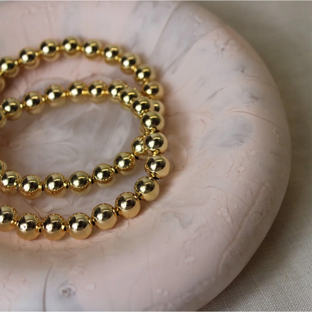 Photo of two gold ball chain bracelets in a pink dish.