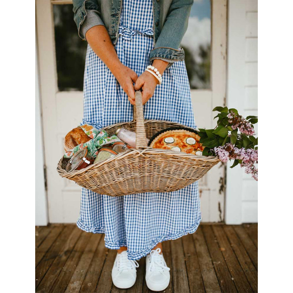 Photo from inside A Basket by the Door recipe book showing lady in a blue gingham dress holding a basket of hamper foods