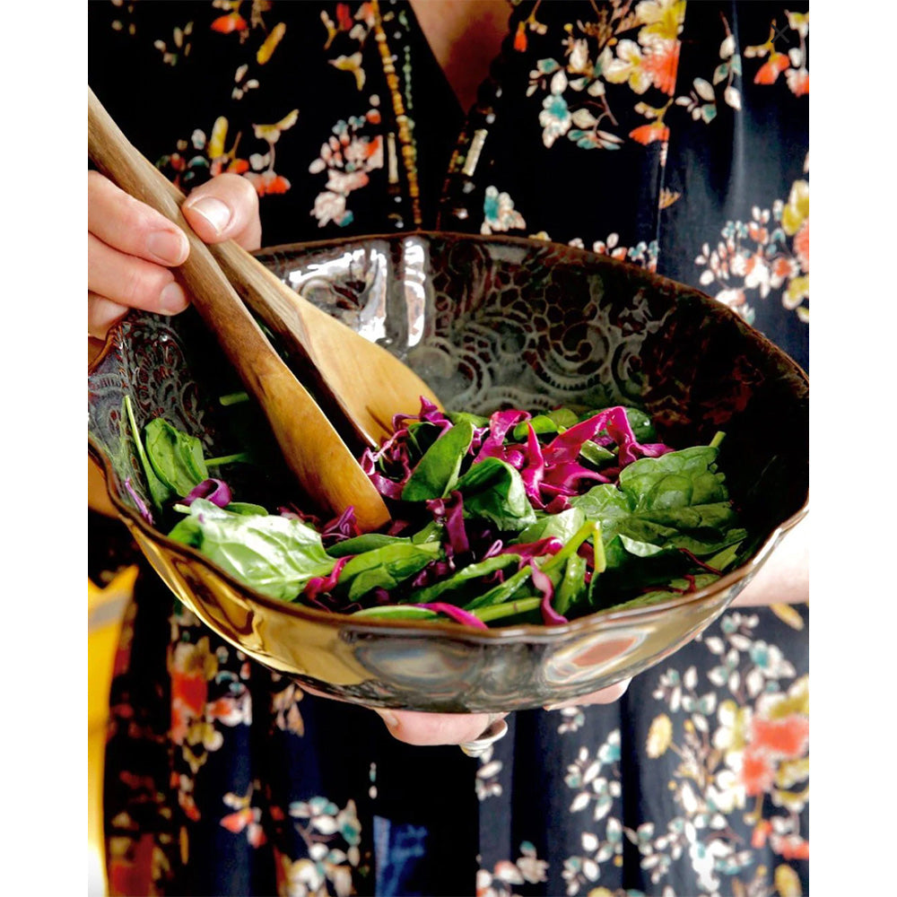 Photo of lady holding a ceramic salad bowl with fluted edges and finished in a dark fig coloured glossy glaze.  There are salad leaves in the bowl and some timber salad servers.