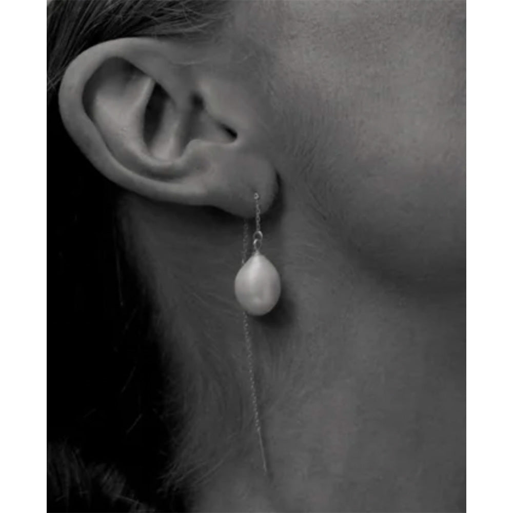 Photo of a chain earring thread with a freshwater pearl at the end.  The photo shows a lady's ear wearing the earring.
