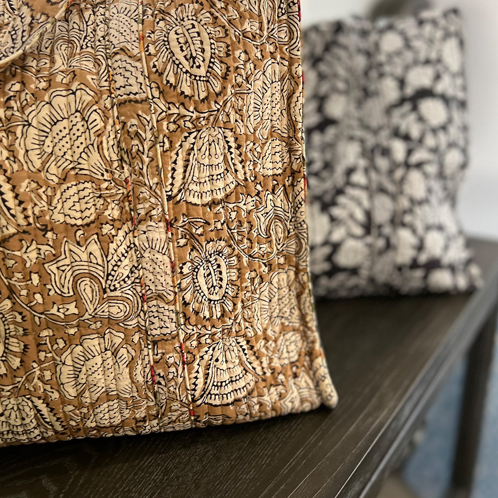 Close up photo of coffee spice floral quilted block printed tote bag sitting on a dark benchtop.  In the distance there is the dark charcoal blue quilted tote.