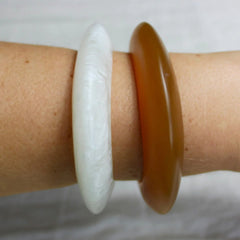 Close up photo of a lady's arm wearing one white and one brown resin bracelet.