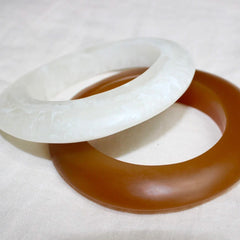 Photo of two resin bracelets, one brown and there is a white bracelet sitting on an angle on top of it.