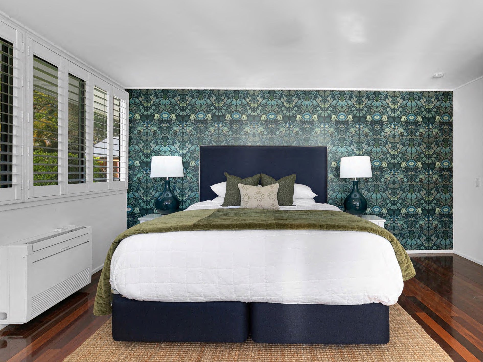 Photo of a bedroom styled by Rachel Elizabeth Interiors showing a deep olive green floral wallpaper feature wall behind navy blue upholstered bed with white bedspread and olive green velvet throw and feature cushions.
