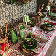 Photo of a Christmas table setting with a cotton tablecloth and napkins in white, red and deep burgundy red floral fabric.  On the table are green bowls, dark rattan placemats, two green and white battery operated table lights and two twig reindeer table ornaments.