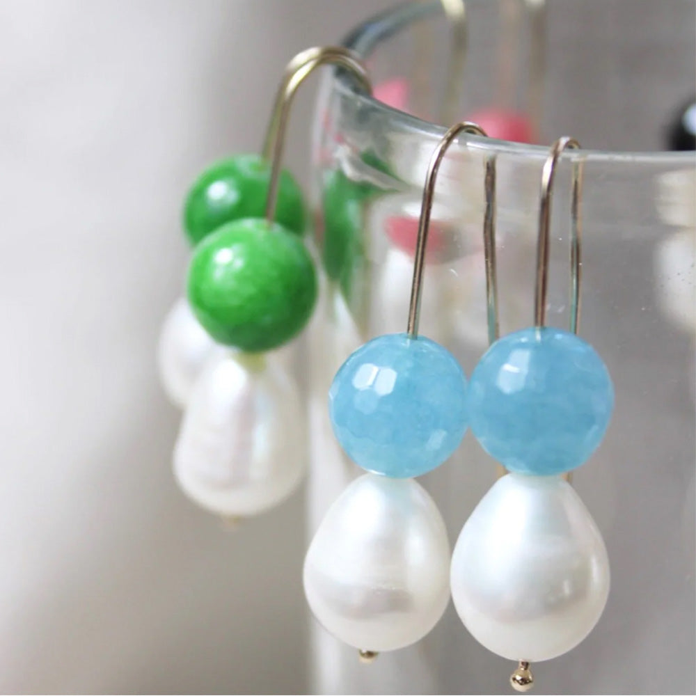 Photo of gold plated hook earrings with a pale blue cut glass-look agate ball and pearl. The earrings are hanging over the side of a glass.