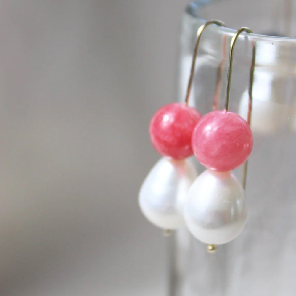 Photo of gold plated hook earrings with a pink agate ball and pearl. The earrings are hanging over the side of a glass.
