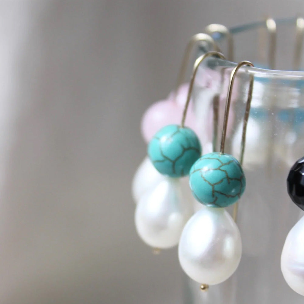 Photo of gold plated hook earrings with a turquoise agate ball which has a crackled finish effect and pearl. The earrings are hanging over the side of a glass.