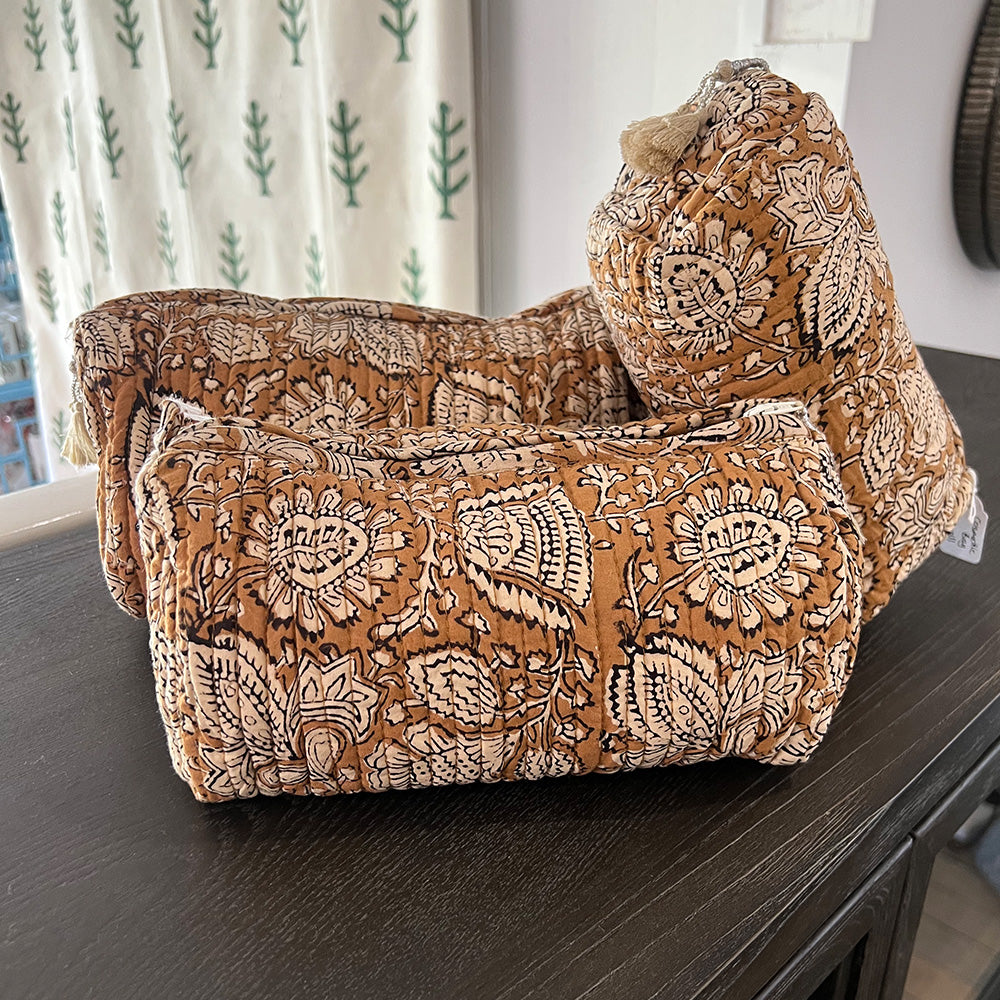 Photo of three coffee spice floral quilted cosmetic pouches showing the three different sizes, and sitting on a dark bench.