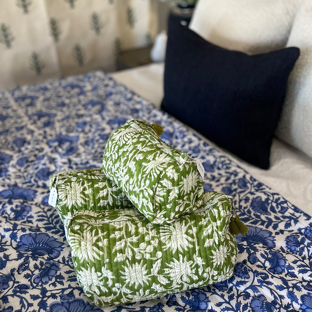 Photo of three forest green floral quilted cosmetic pouches showing the three different sizes, and sitting on a blue floral quilt.