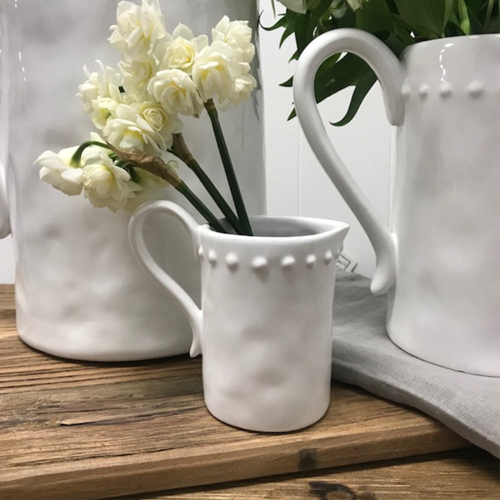 Close up of small white shiny ceramic jug with dot detail around the top outside edge and flowers sitting in the jug showing it used as a vase