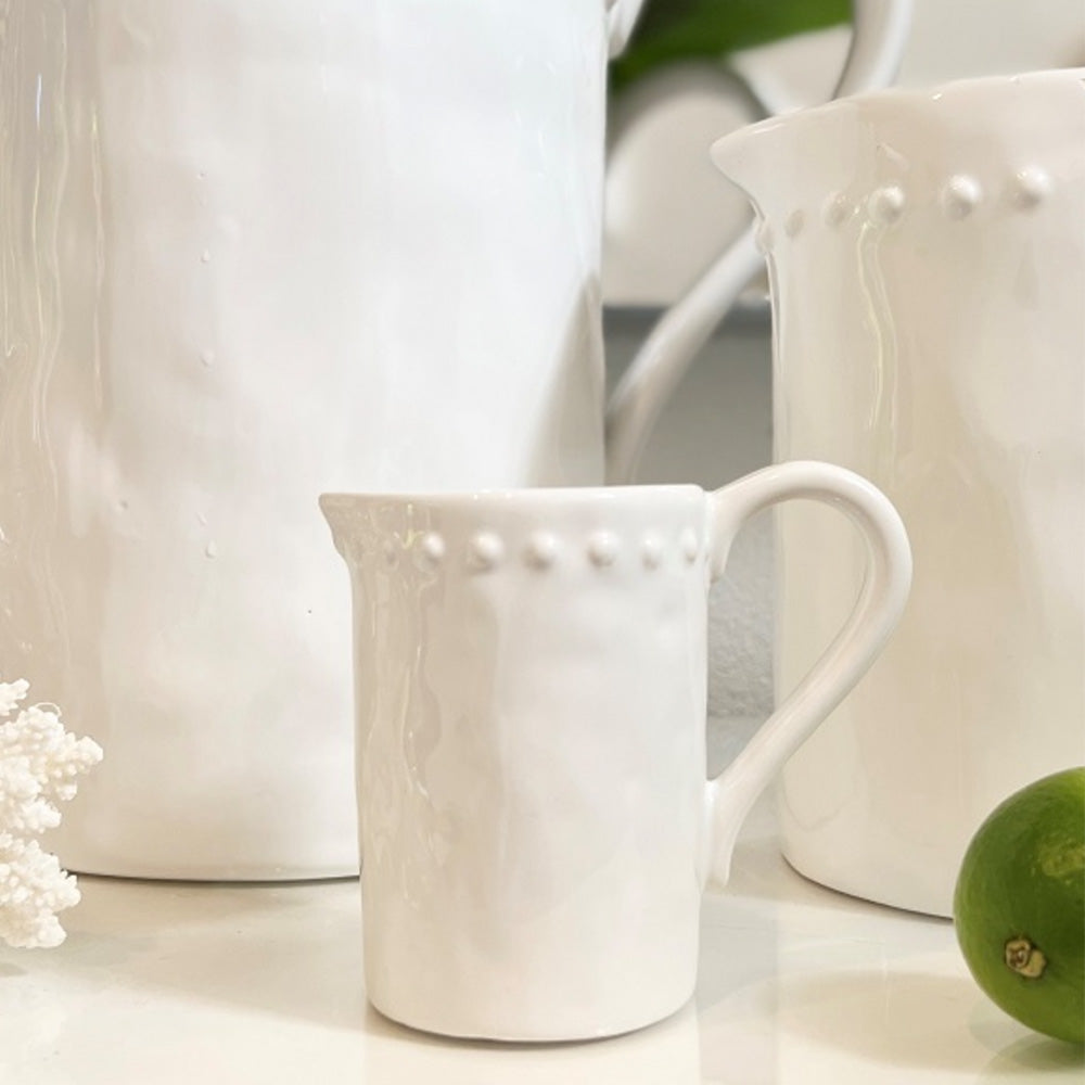 Close up of small white shiny ceramic jug with dot detail around the top outside edge