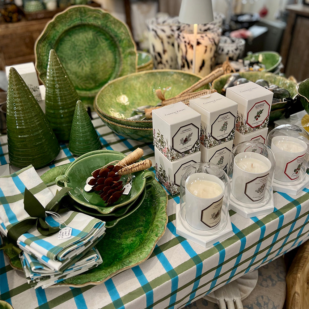 Photo of a white, aqua blue and olive green check fabric cotton tablecloth on a table with items on top of the table such as green bowls and plates, candles and matching white, aqua and olive green folded napkin sets.
