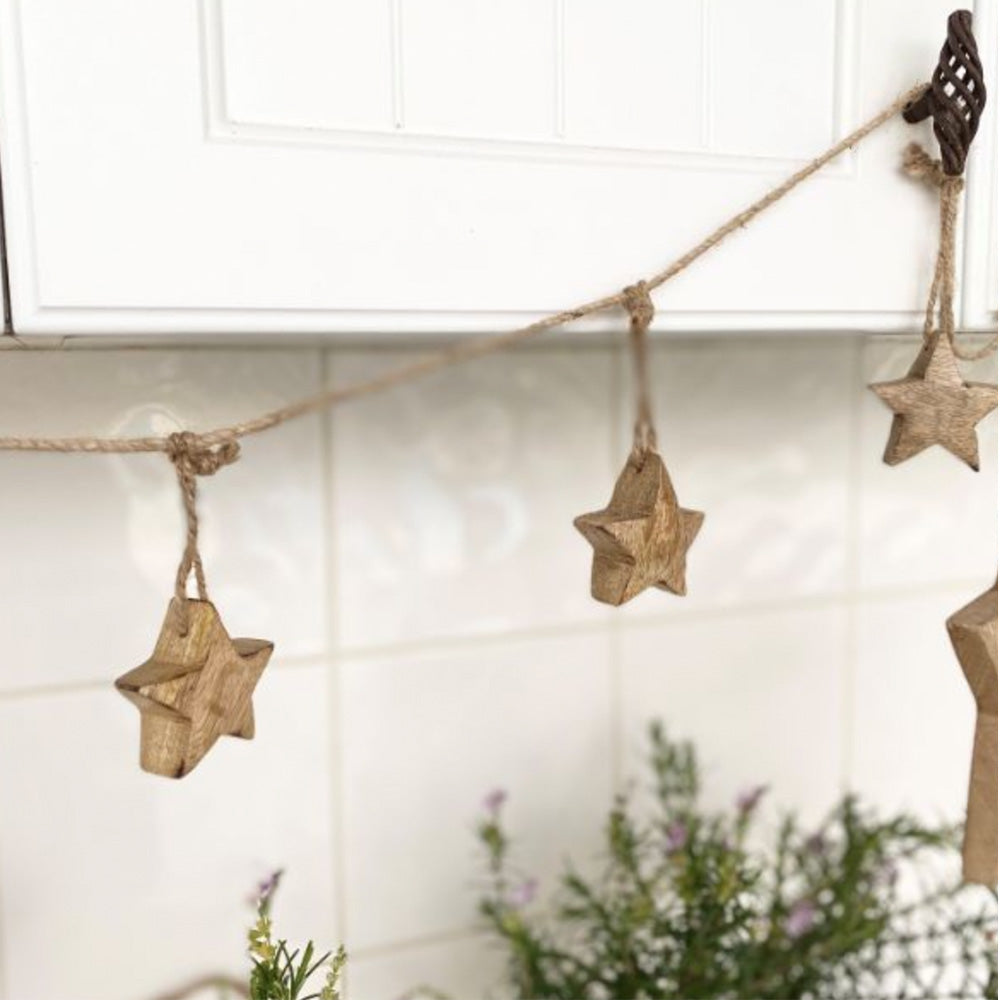 Solid timber stars hanging on a rope garland as a Christmas decoration, hanging from metal cupboard handles on a white kitchen cupboard.