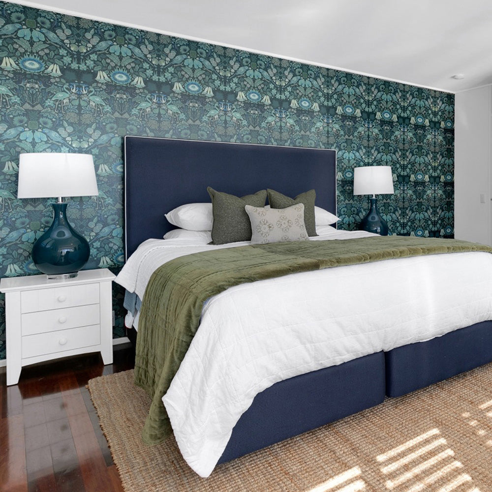 Photo of a bedroom styled by Rachel Elizabeth Interiors showing a deep olive green floral wallpaper feature wall behind navy blue upholstered bed with white bedspread and olive green velvet throw and feature cushions.