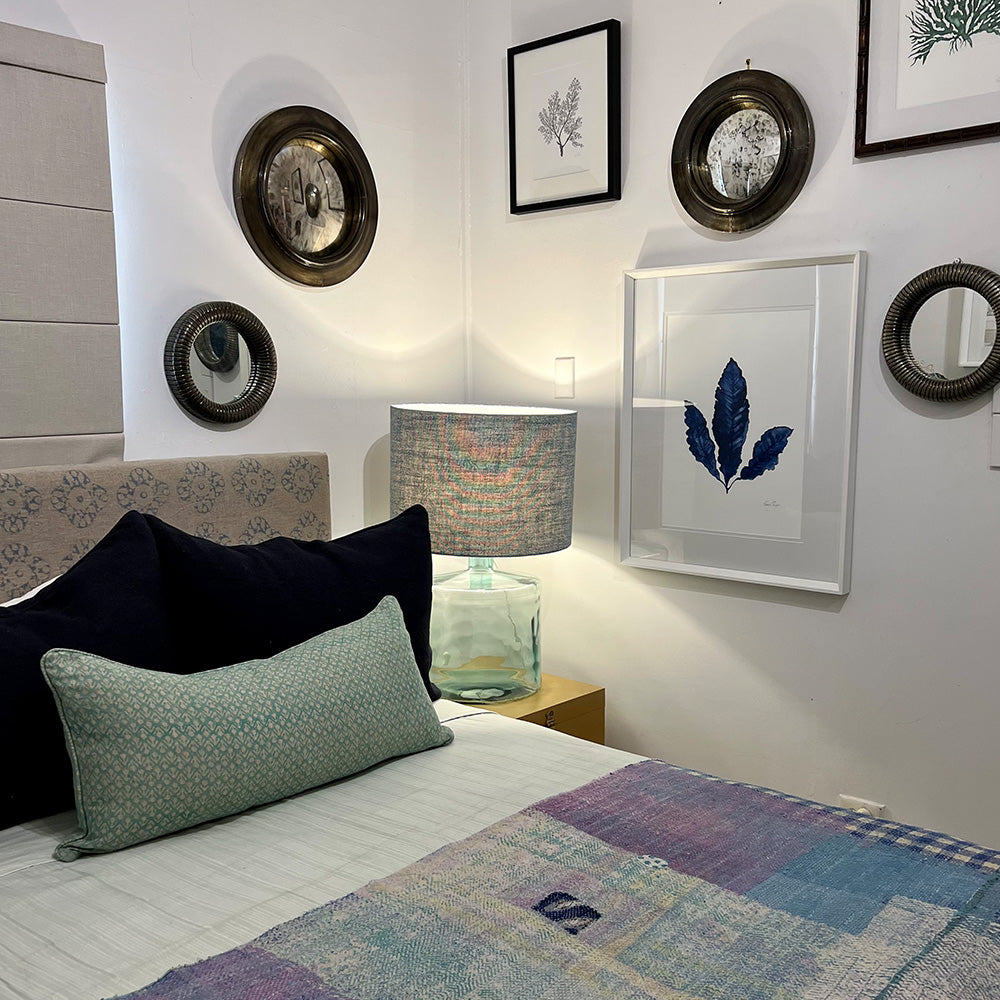 Photo of antique convex mirrors on bedroom wall beside artwork and above bed and bedside table