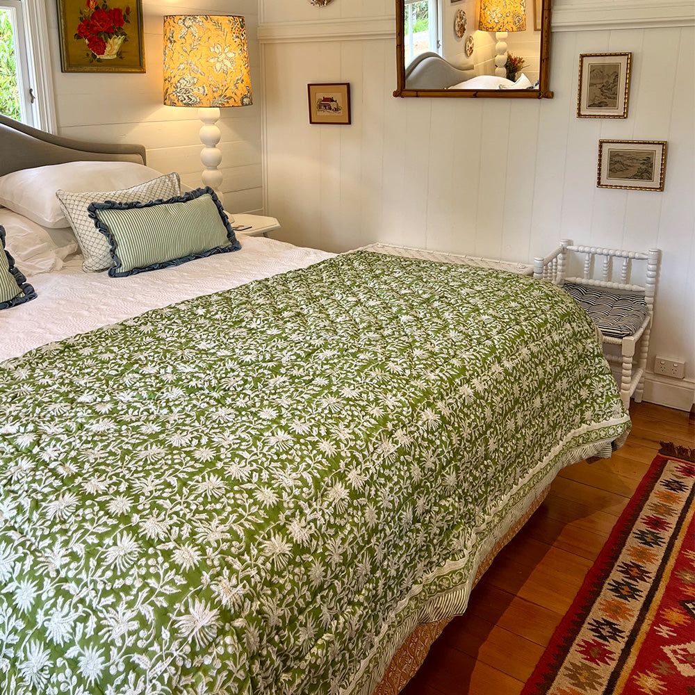 Photo of a forest green and white floral quilted bedspread over the end of a bed.