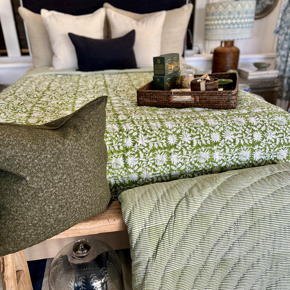 Photo of a forest green and white floral quilted bedspread over a bed.  At the end of the bed is a bench with the reverse side of the quilt in forest green and white stripe quilt folded over the bench, sitting beside an olive green boucle cushion.