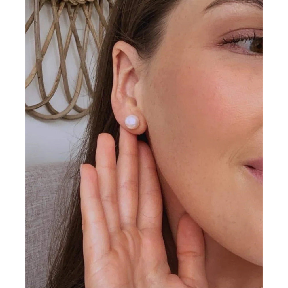 Photo of the side of a woman's face with her hand up to her ear lobe showing the pearl stud earring.