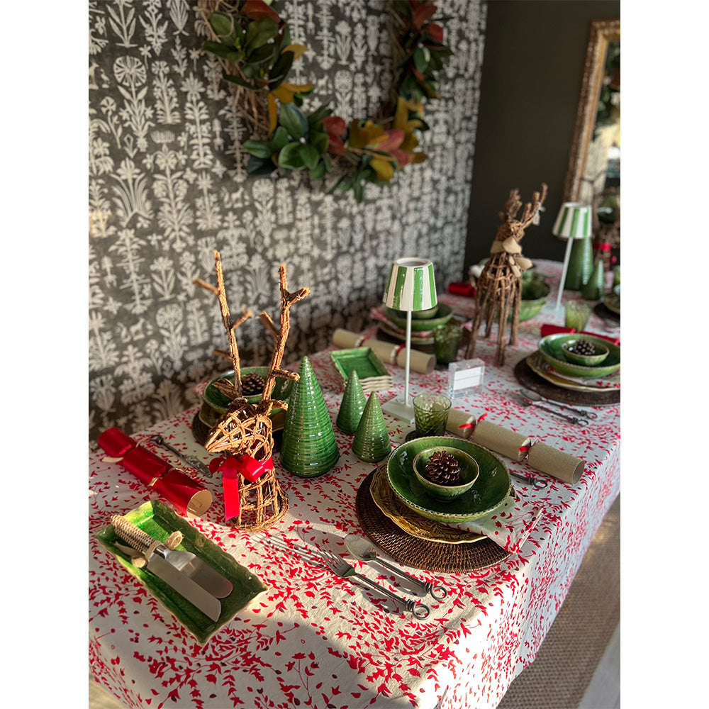 Photo of a Christmas table setting with a cotton tablecloth and napkins in white, red and deep burgundy red floral fabric.  On the table are green bowls, dark rattan placemats, two green and white battery operated table lights and two twig reindeer table ornaments.