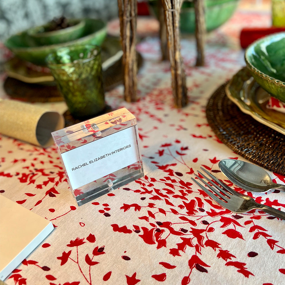 Close up photo of a Christmas table setting with a cotton tablecloth in white, red and deep burgundy red floral fabric.  There is also a close up photo of Rachel Elizabeth Interiors business card in a perspex frame sitting on the tablecloth.