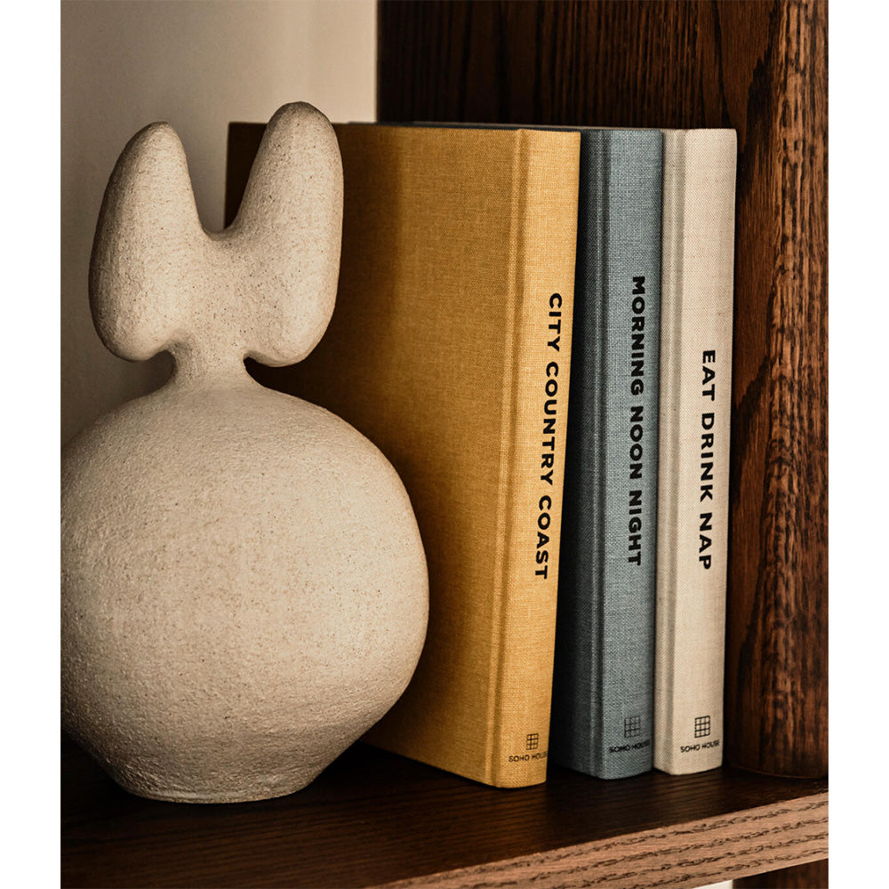 Photo of a bookshelf showing the three Soho House books, City County Coast, Morning Noon Night and Eat Drink Nap.  There is a large neutral vase being used as a bookend.