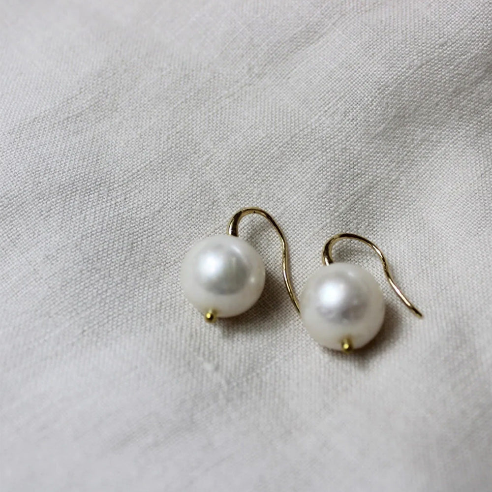 Close up photo of gold hook earrings with large round pearls.