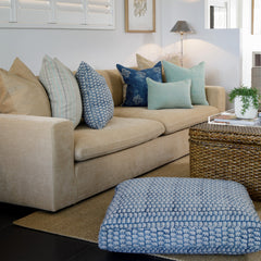 Photo of block printed Hastin in Blue linen floor cushion sitting beside rattan coffee table and mustard coloured sofa