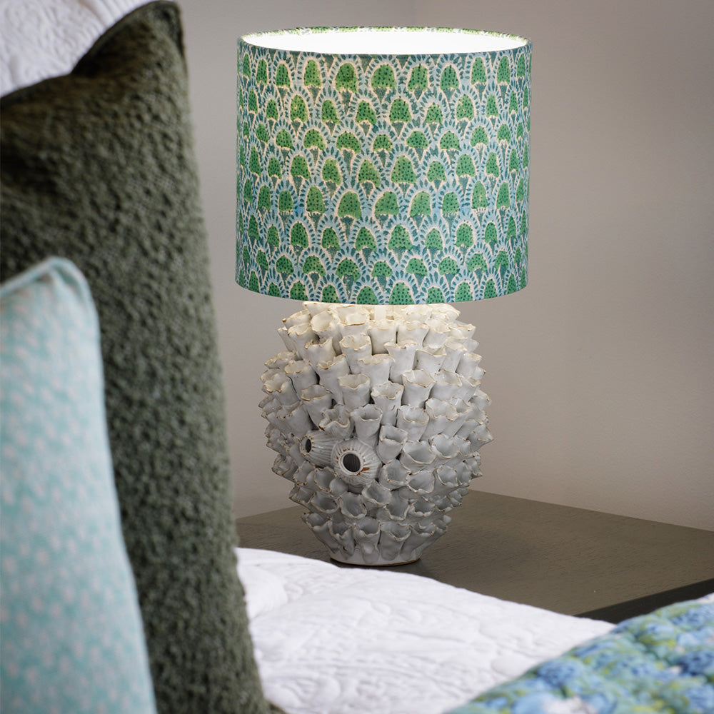 Photo of olive green boucle cushion on a bed beside a green and white bedside lamp