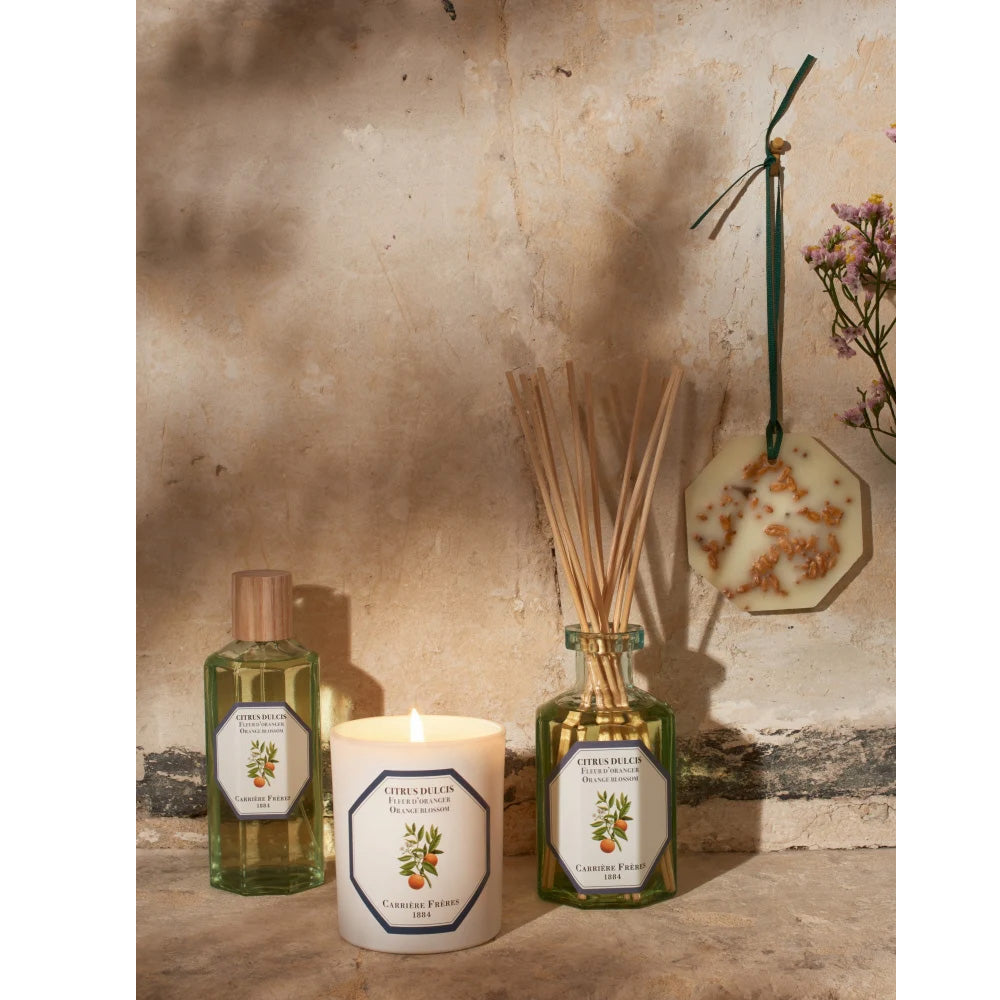Photo of orange blossom scented room spray, candle and room diffuser bottle and sticks made by Carriere Freres, as well as an orange blossom scented wax palet hanging on the wall.