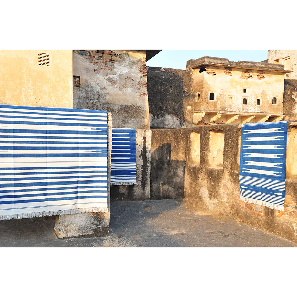 Photo of blue and white Arizona cotton dhurrie rugs hanging over stone walls